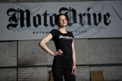 Женщина в футболке MotoDrive на фоне вывески мотошколы
